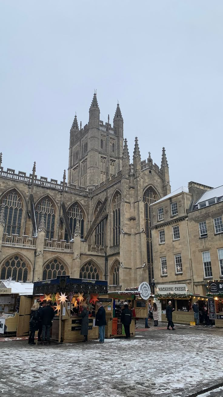 people are standing in front of an old building on a snowy day with christmas decorations