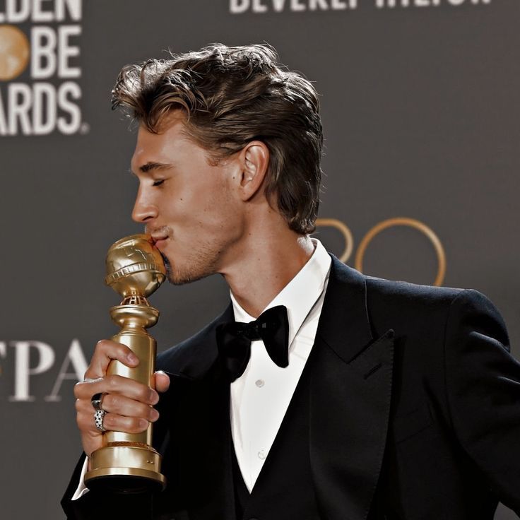 a man in a tuxedo holding an award for best performance by an actor