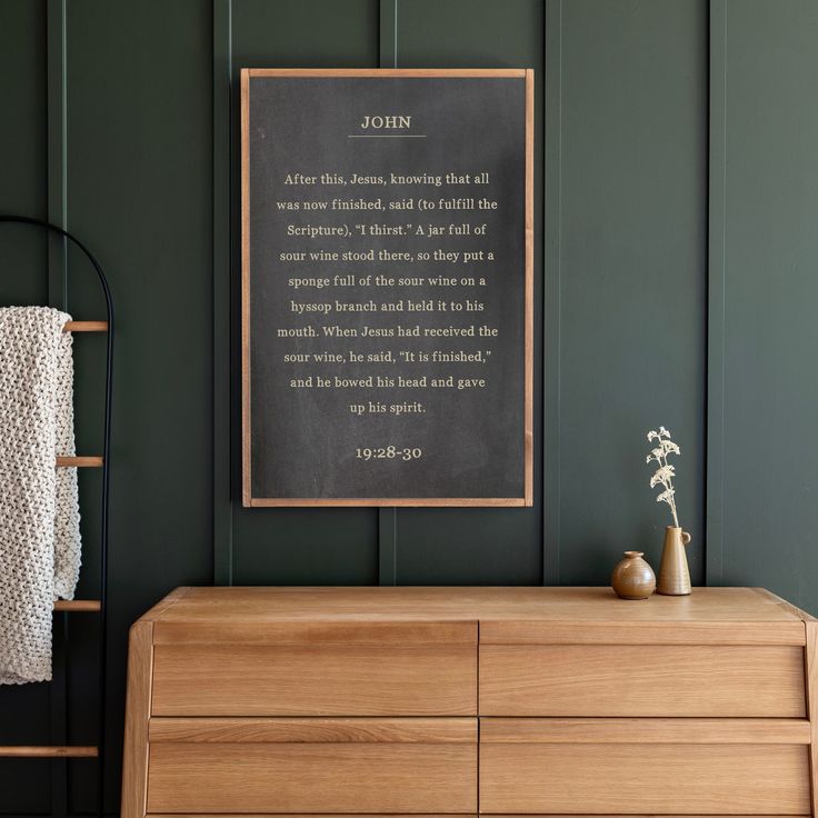 a wooden dresser sitting next to a green wall with a framed poem on the wall