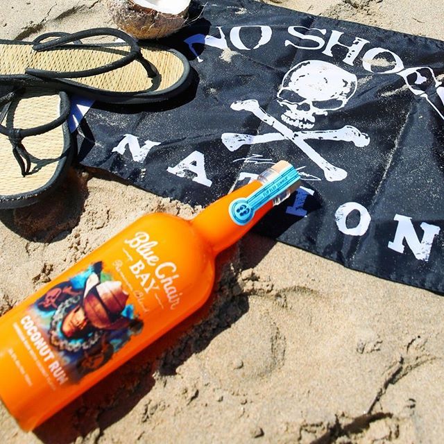 an orange toothbrush sitting on top of a beach next to a black pirate flag