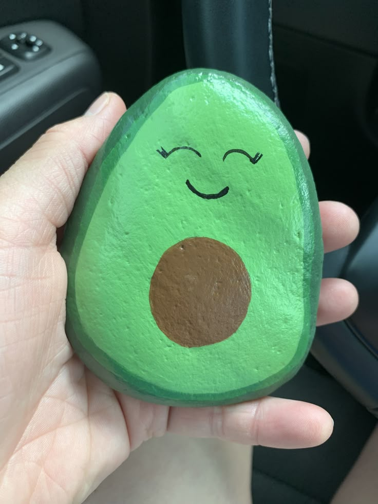 a hand holding a green rock with a smiling face painted on it's side