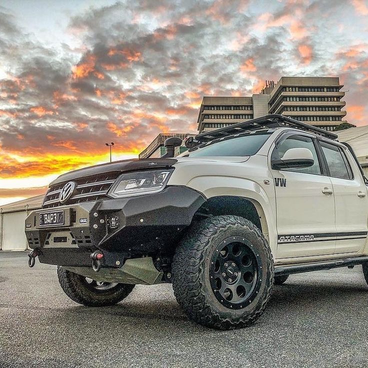 a white truck parked on top of a parking lot next to a tall building at sunset