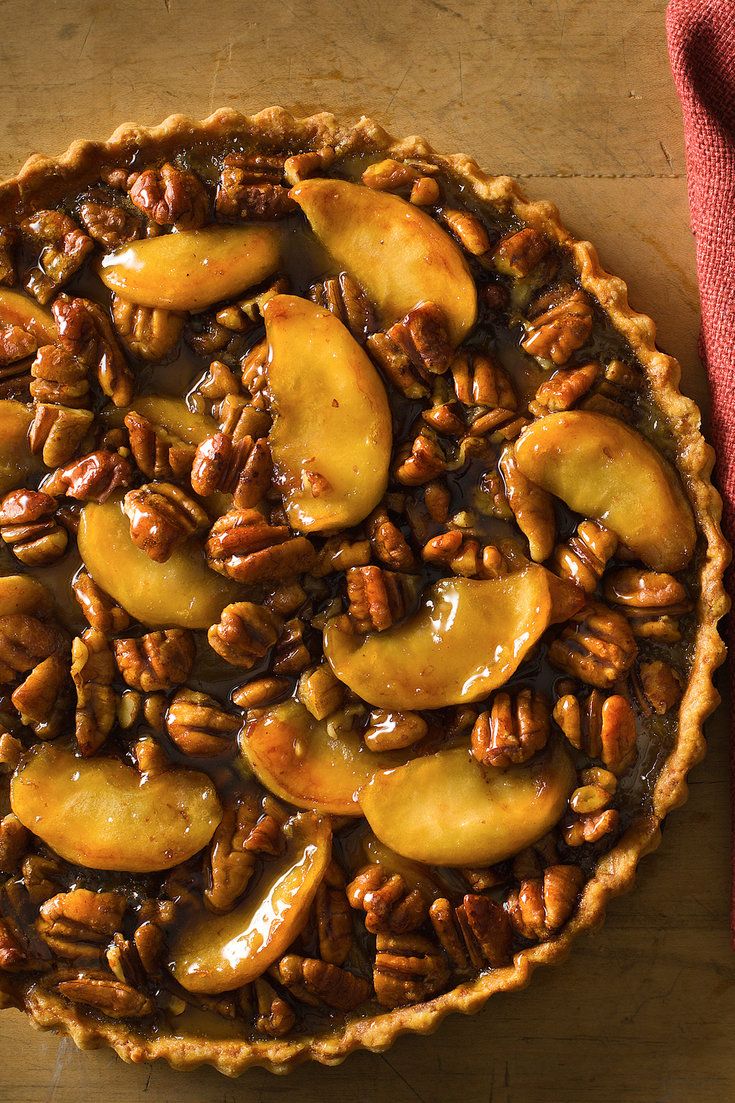 a pie with pecans and caramel on top sitting on a wooden table next to a red napkin