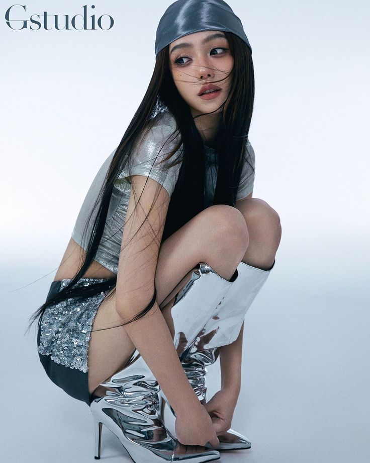 a woman in silver is posing for a magazine cover with her legs crossed and heels on the ground