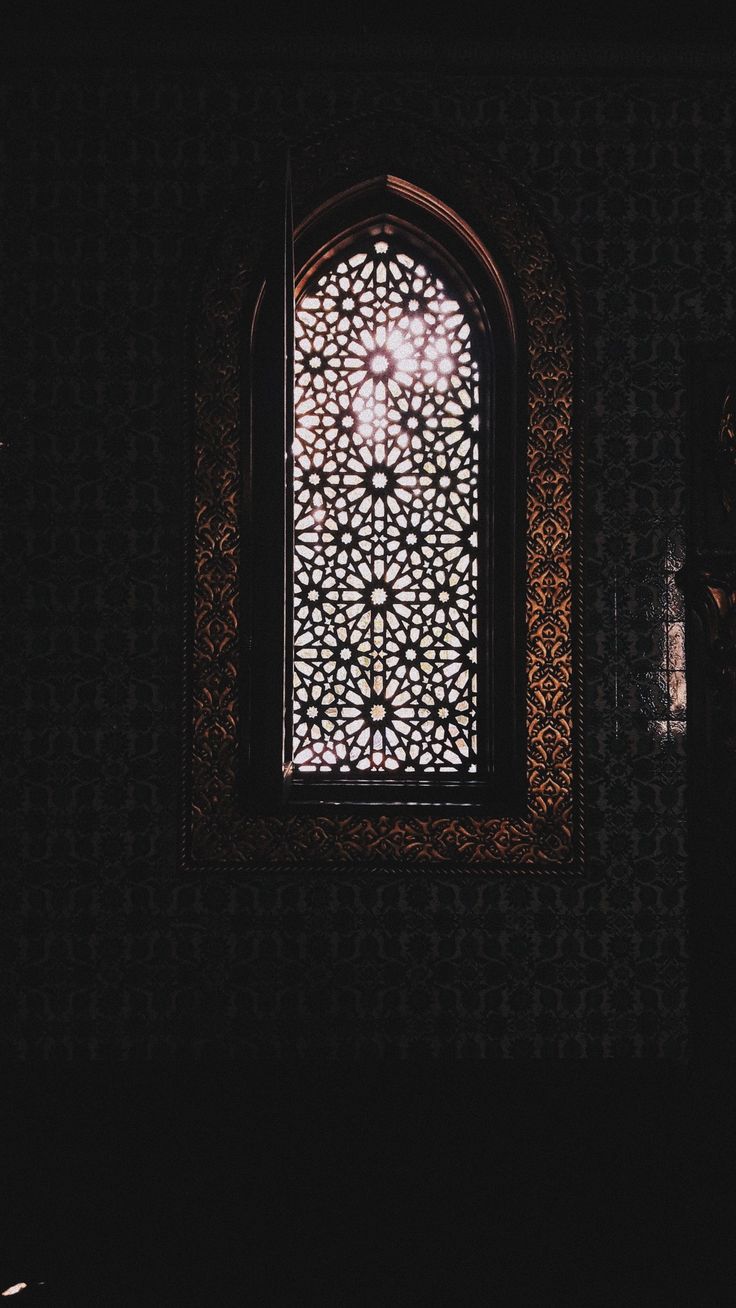 an ornate window in a dark room with the light coming through it's opening