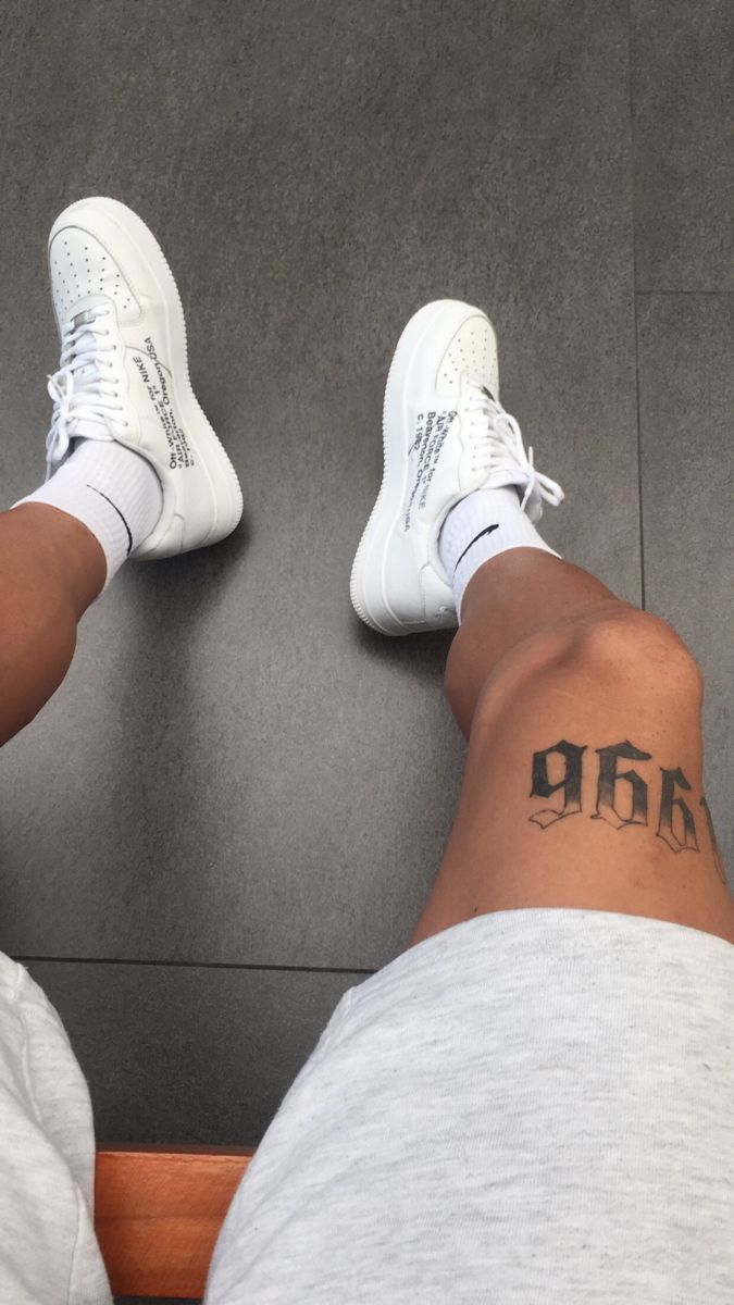 a person with a tattoo on their left leg and white tennis shoes sitting next to each other