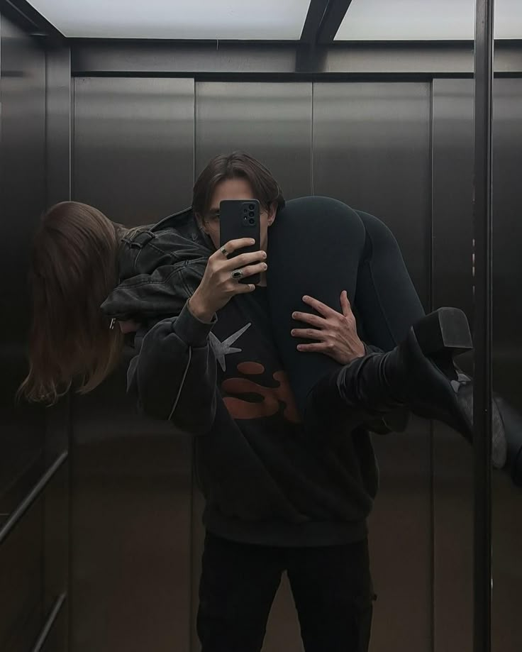 a man taking a selfie with his cell phone in an elevator while another person takes a photo