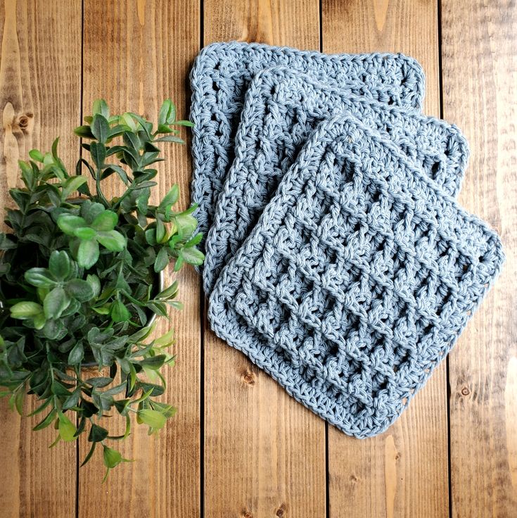 three crocheted coasters sitting on top of a wooden table next to a potted plant