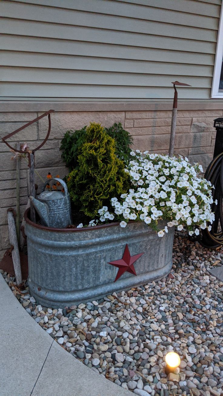 a metal tub filled with white flowers next to a sidewalk and bike parked in front of a house