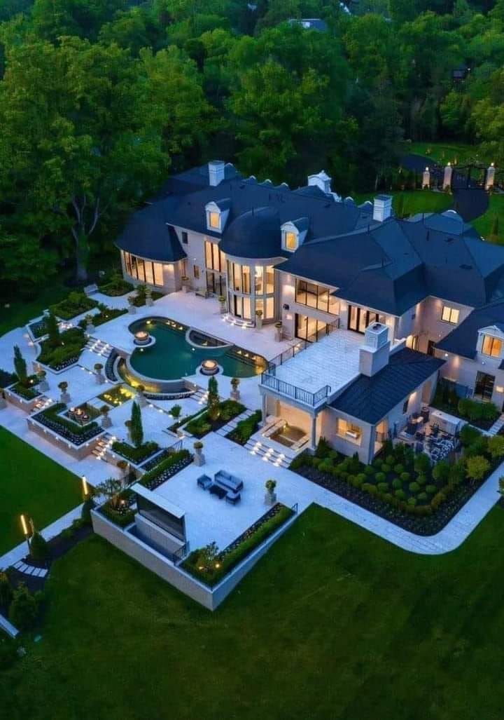 an aerial view of a large mansion with pool in the foreground and landscaping around it