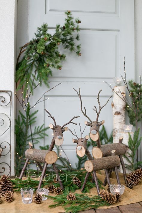 three reindeer figurines sitting on top of a table next to pine cones and evergreen branches