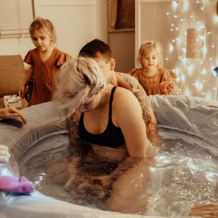 a group of people in a hot tub with water on the floor and one woman holding a baby