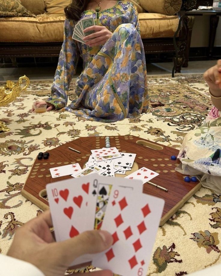 a woman sitting on the floor playing cards with another person holding one card in front of her