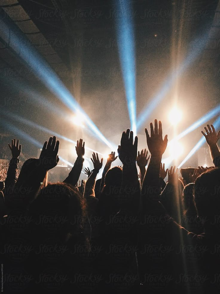 a crowd at a concert with their hands in the air and lights shining down on them