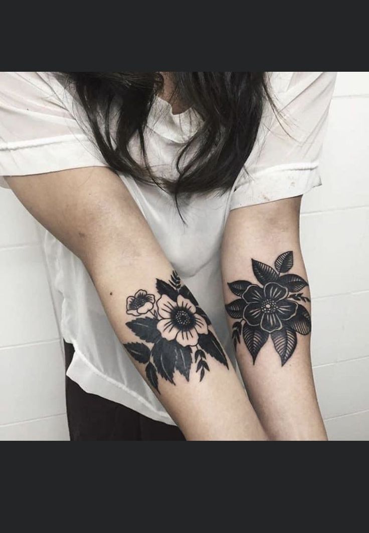 two black and white tattoos on both arms, one is holding the other's arm