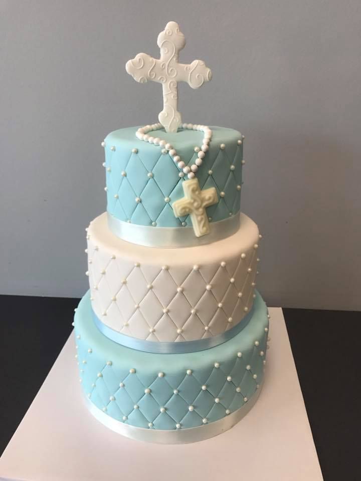 a three tiered cake decorated with blue and white fondant, pearls and a cross on top