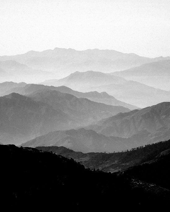 black and white photograph of mountains with fog in the air, taken from an overlook point