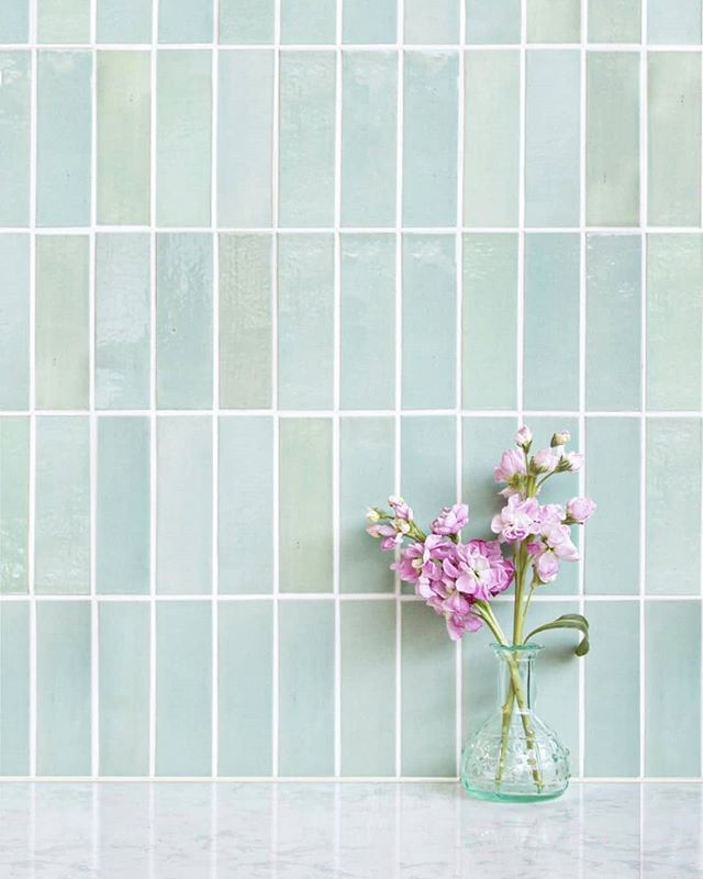 a glass vase with flowers in it on a counter top next to a tiled wall