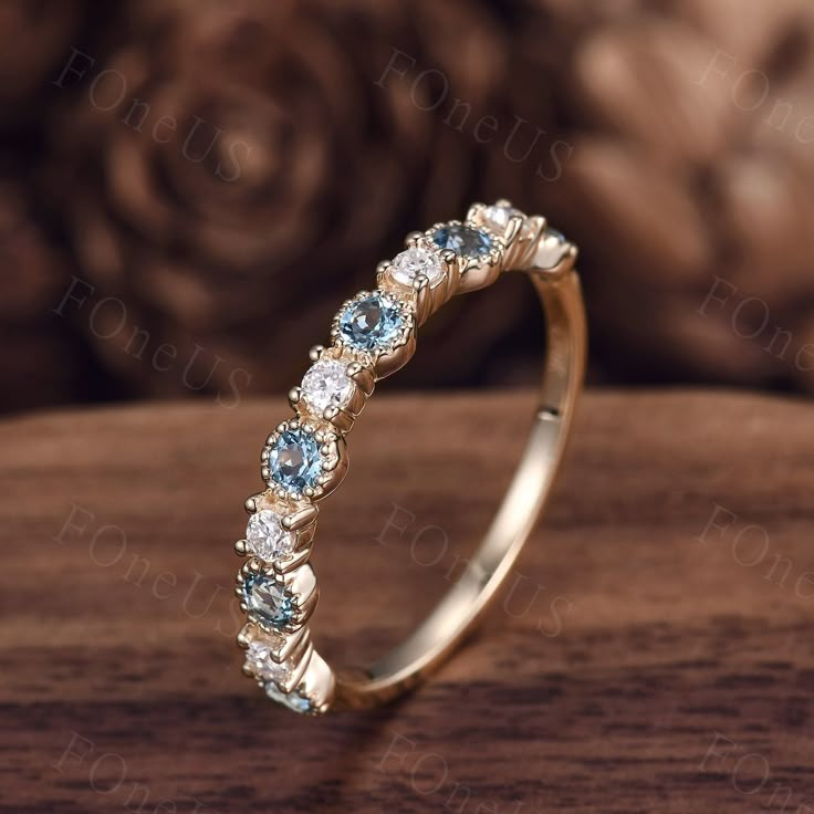 a gold ring with blue and white stones on it sitting on a wooden table next to roses