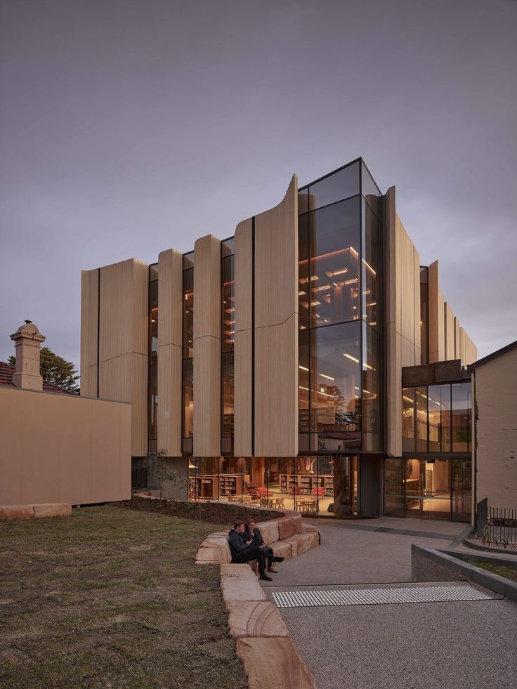 a person sitting on a bench in front of a building with glass walls and windows