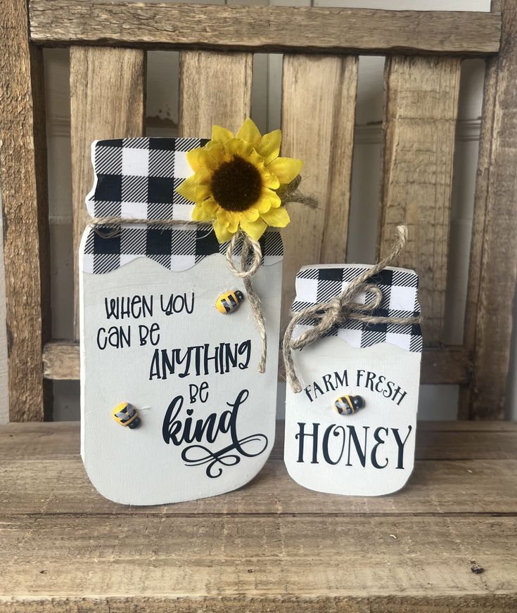 two painted mason jars sitting on top of a wooden bench next to a sunflower