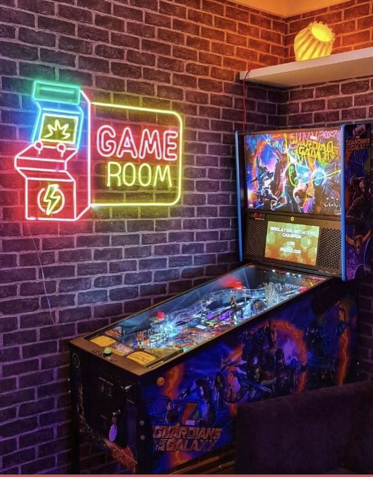 a pinball machine sitting in front of a brick wall with neon signs on it