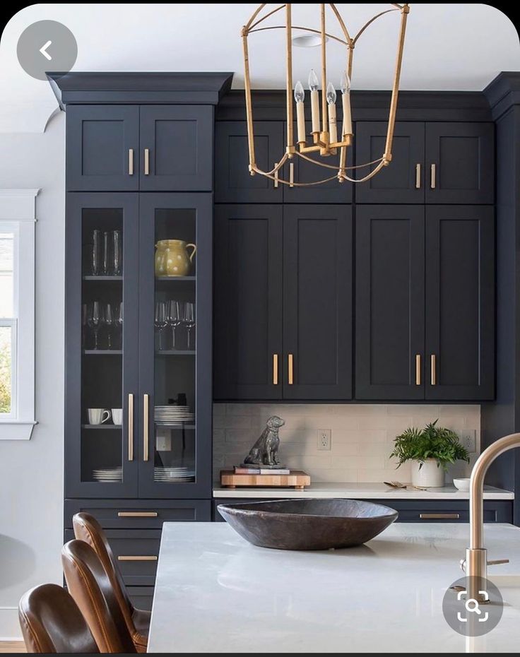 a modern kitchen with black cabinets and white counter tops, gold chandelier hanging from the ceiling