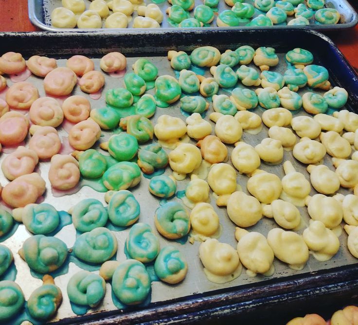 there are many different colored cookies on the trays and one is green, yellow, and blue