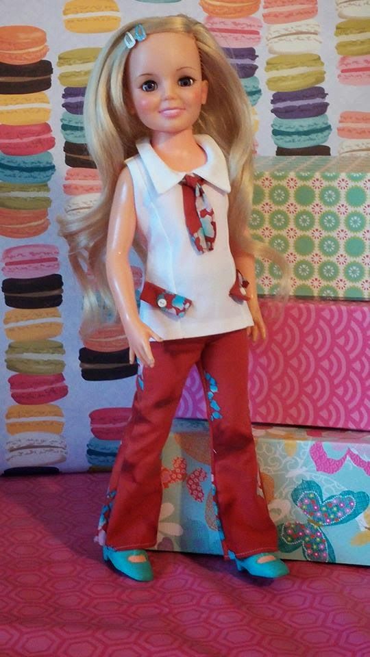 a doll with blonde hair wearing red pants and a white shirt is standing in front of a colorful wall