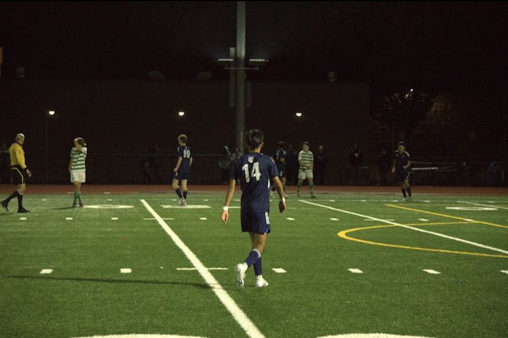 a group of people playing soccer on a field at night with the lights turned on