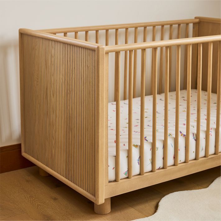 a wooden crib with white sheets in a room