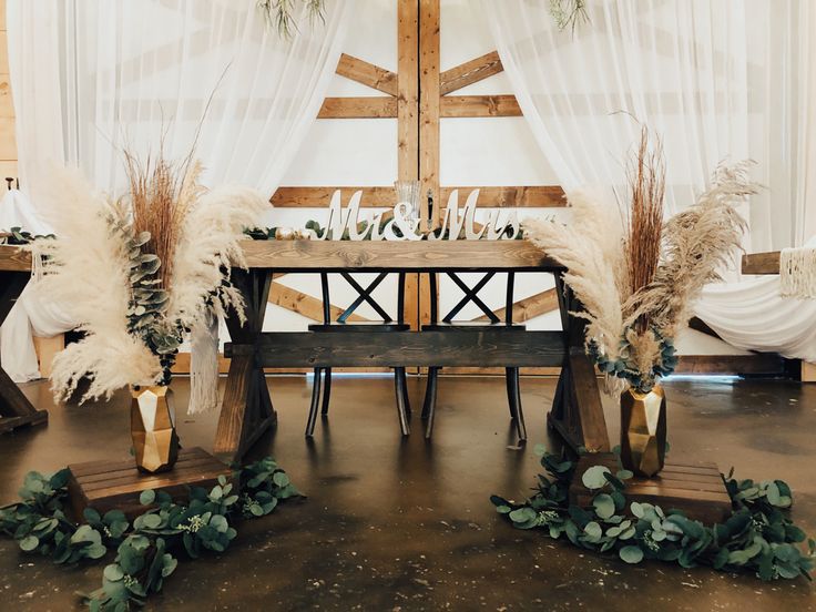 a wooden table topped with lots of white flowers and greenery next to a bench