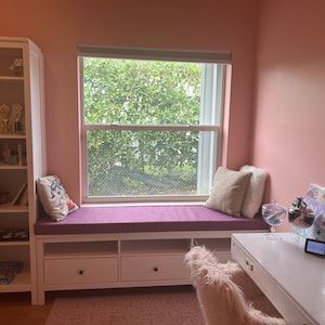 a room with a window seat, desk and bookshelf next to the window