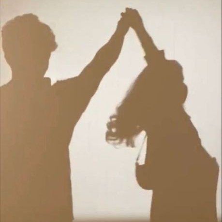 two people standing in front of a white wall with their hands up to each other