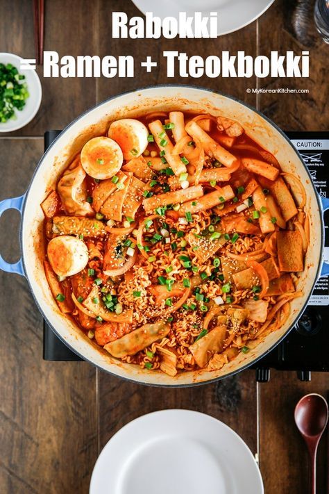 a large pot filled with food sitting on top of a wooden table next to plates and utensils