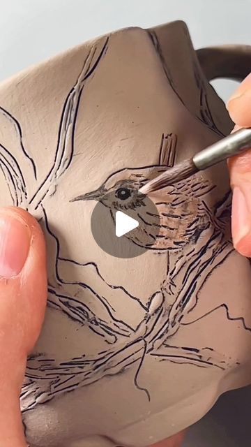 a person is painting a bird on a clay bowl with a brush and glue pen