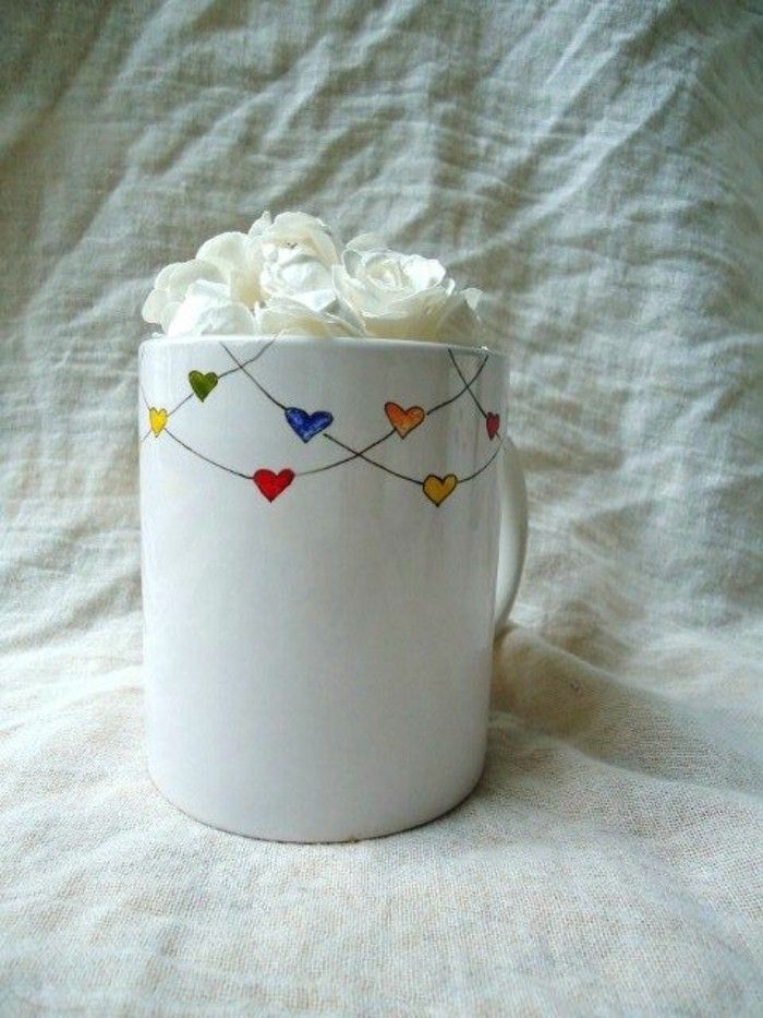 a white coffee cup filled with roses on top of a bed covered in white sheets