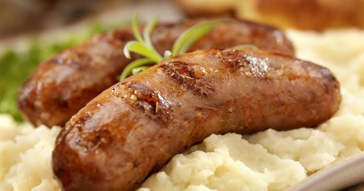 two sausages on top of mashed potatoes and garnished with green sprigs