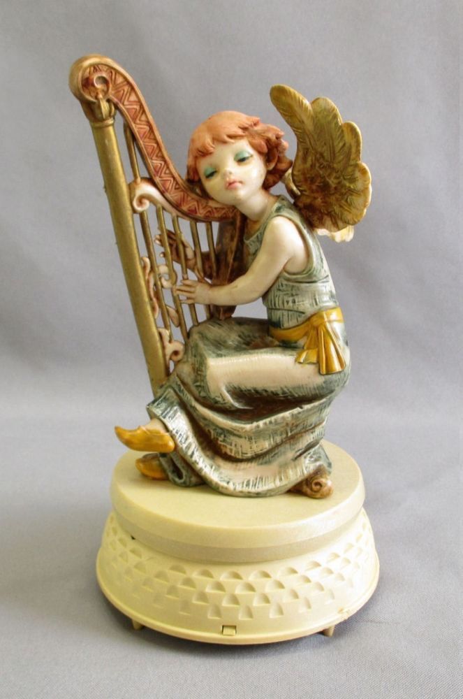 an angel figurine sitting on top of a white base with a harp in it's hands