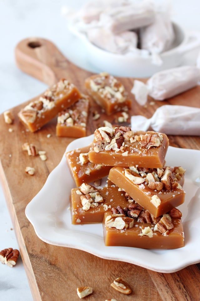 several pieces of caramel and walnut fudge on a white plate next to a wooden cutting board