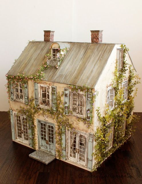 a doll house with ivy growing on the roof and windows, in front of a white wall