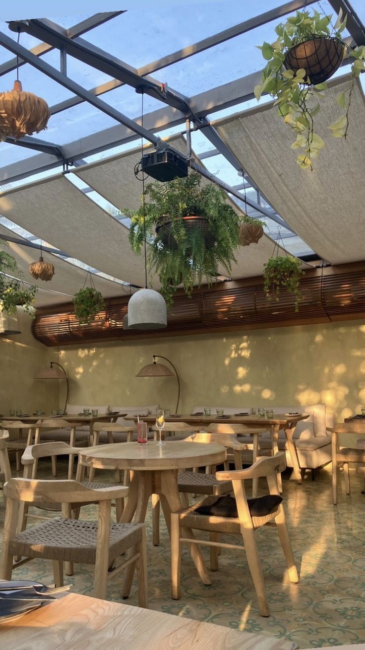 an outdoor restaurant with tables and chairs under a glass roof covered in potted plants