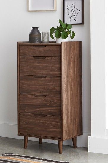 a wooden dresser sitting next to a wall with pictures on the wall and a vase