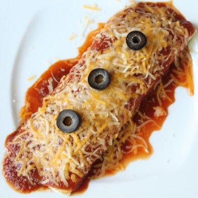 an enchilada covered in cheese and olives on a plate with eyes