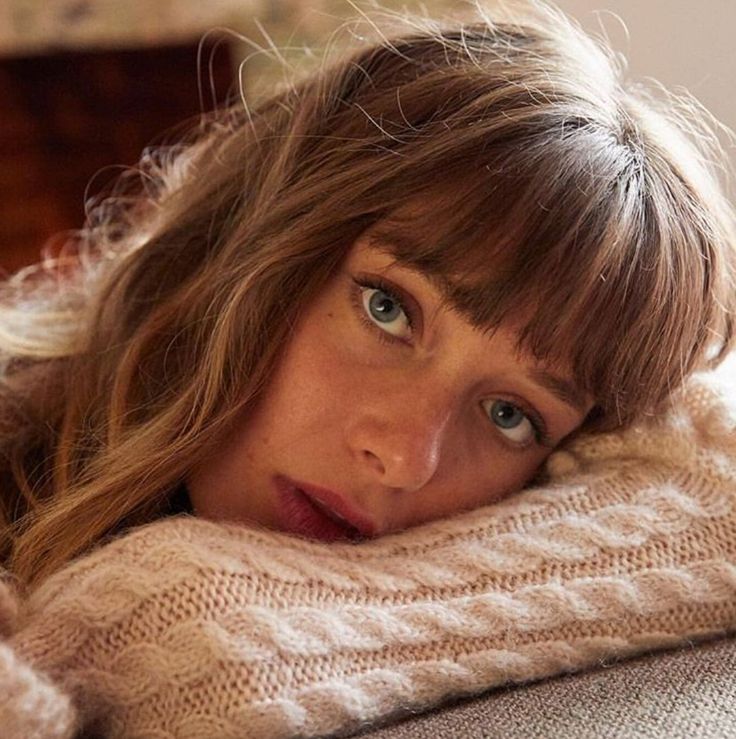 a woman laying on top of a couch covered in a white blanket and looking at the camera