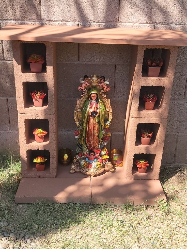 an outdoor shrine with many pots and plants on it's sides, in front of a brick wall