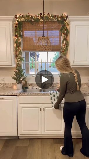 a woman standing in front of a kitchen counter with christmas decorations on the window sill