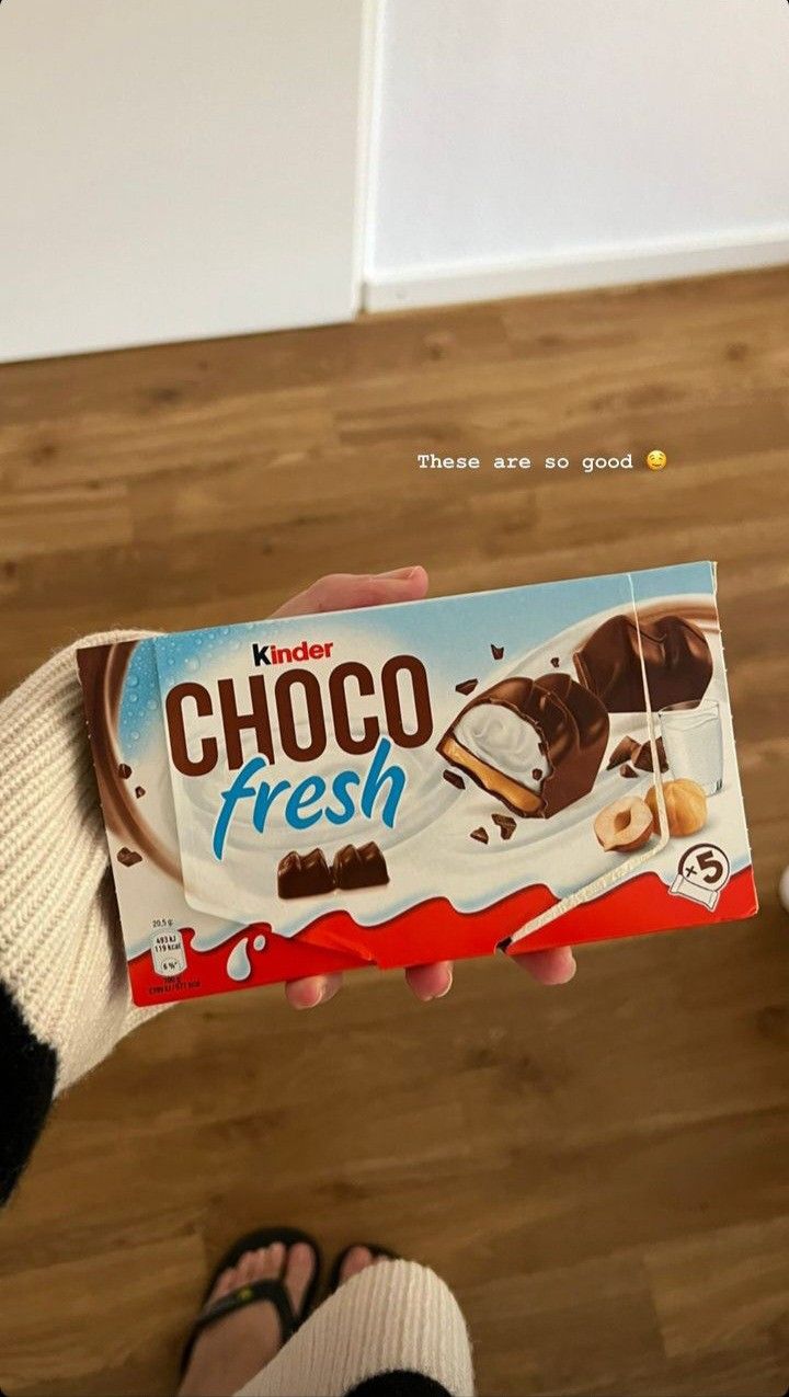 a person holding up a box of chocolate fresh with their feet on the floor in front of them