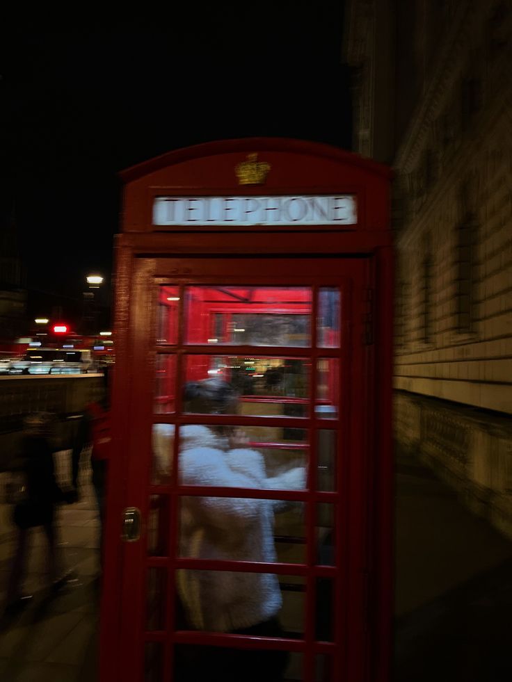 a red phone booth sitting on the side of a road next to a building at night