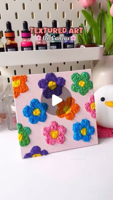 an art project with crochet flowers and a penguin on the table next to it